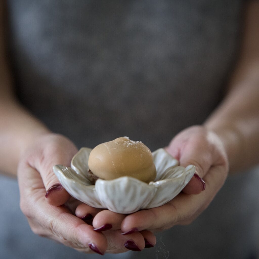 Handgjort dekorationsfat Ingrid i offwhite porslin med litet ljus, hålls i händer