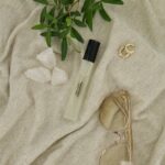 Eau de Parfum Scent of Purity från Washologi på ljust tyg med växt, glasögon och smycken