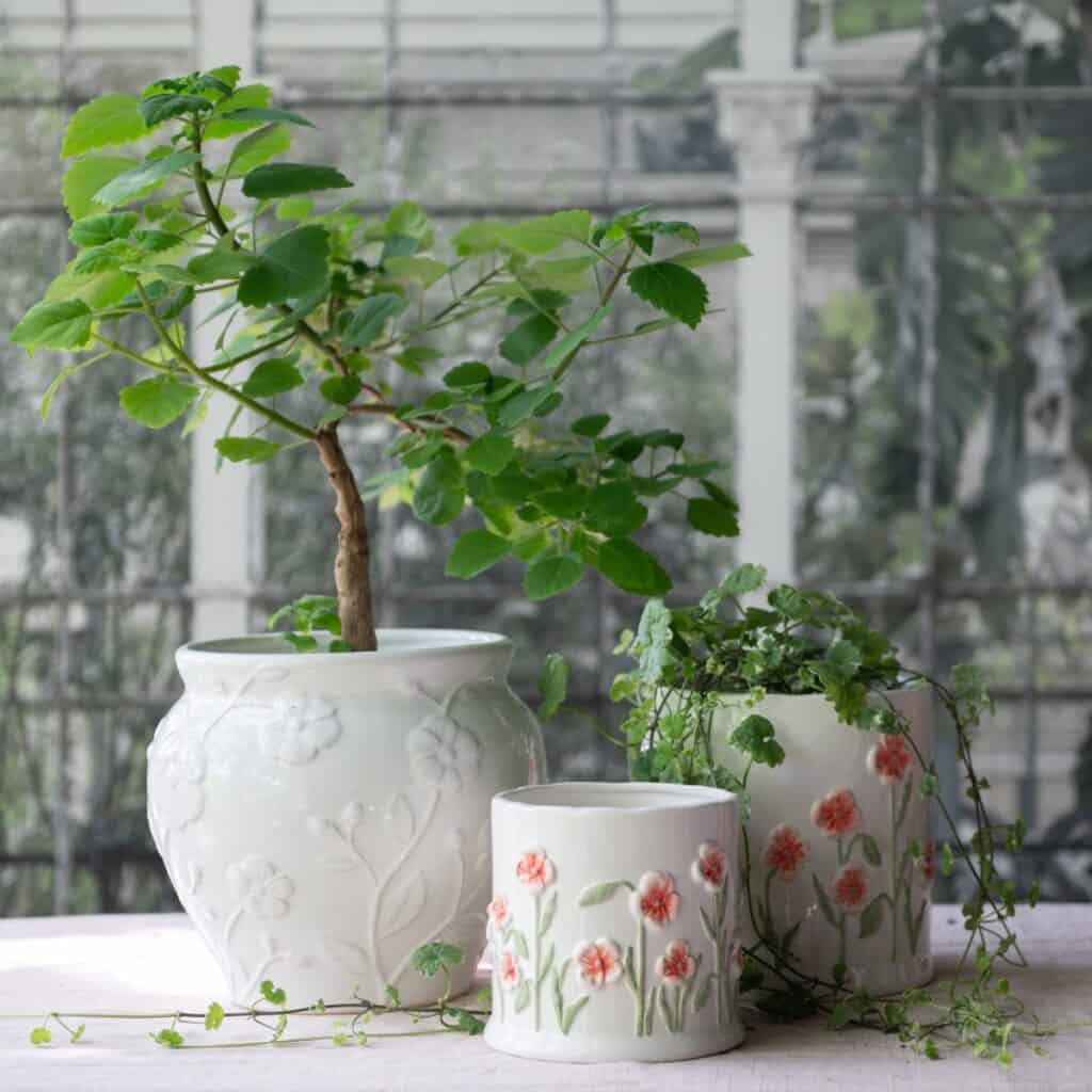 Vit porslinskruka Eliza med blomrelief i miljö med gröna växter på bord