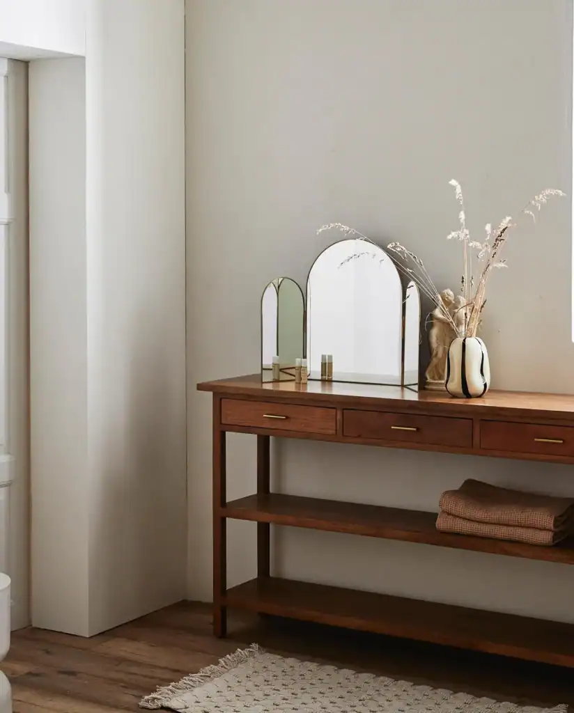 Badrumsmöbel i mörkt trä med speglar i antik mässing, placerad mot ljus vägg med handdukar och naturfärgade detaljer.