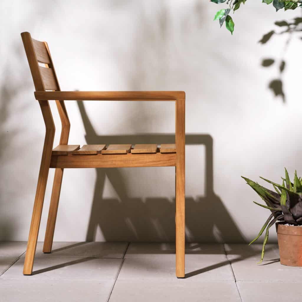 Delia trädgårdsstol i massiv teak med armstöd placerad på uteplats