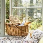 Picknickkorg i pil med blått kylfack placerad i fönster med sommargrönska