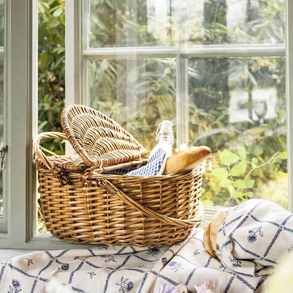 Picknickkorg i pil med blått kylfack placerad i fönster med sommargrönska