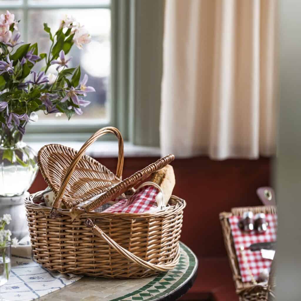 Picknickkorg INA med kylväska i natur och röd på bord vid fönster med blommor