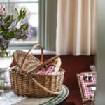 Picknickkorg INA med kylväska i natur och röd på bord vid fönster med blommor