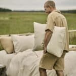 Man bär Pyjamas NICOLA nougat i 100% bomullsmuslin med kortärmad skjorta och shorts utomhus vid bäddad säng