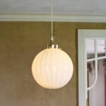 Taklampa Marit i opalglas och mässing som sprider varmt ljus i ett rum