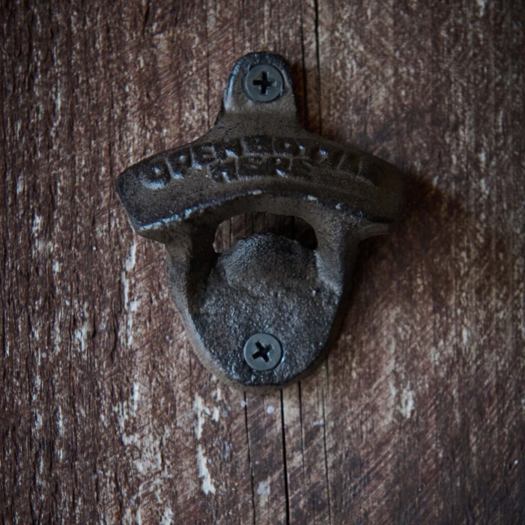 Detaljbild av väggmonterad flasköppnare i brunt järn med rustik patina