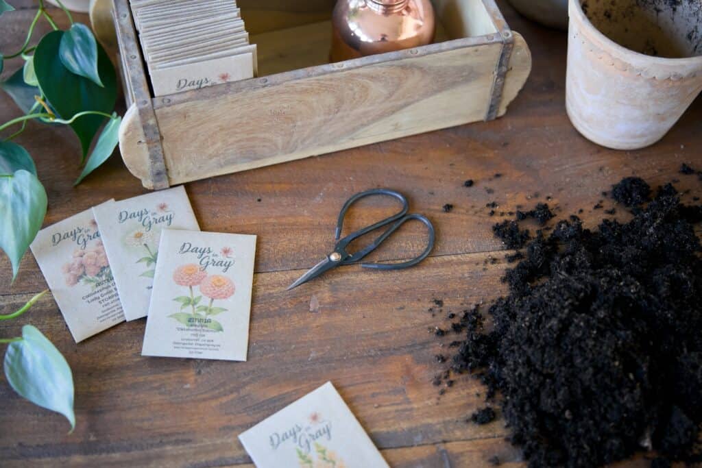 Fröpåsar, planteringsjord och terrakottakrukor på ett bord inför frösådd.