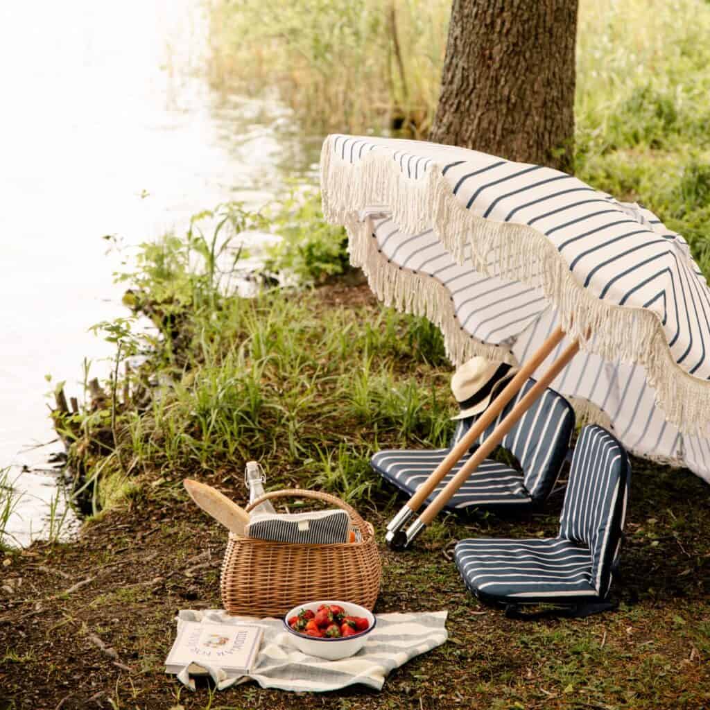 Picknickkorg Molly i pil under somrig picknick vid sjön med parasoll och sittdynor