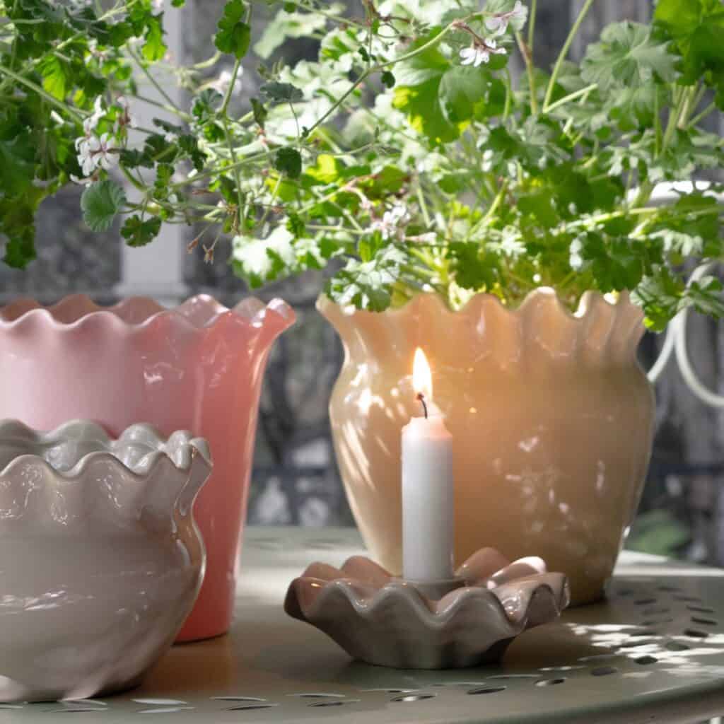 EVELINA ljusstake och blomkrukor med vågig kant på trädgårdsbord med gröna växter