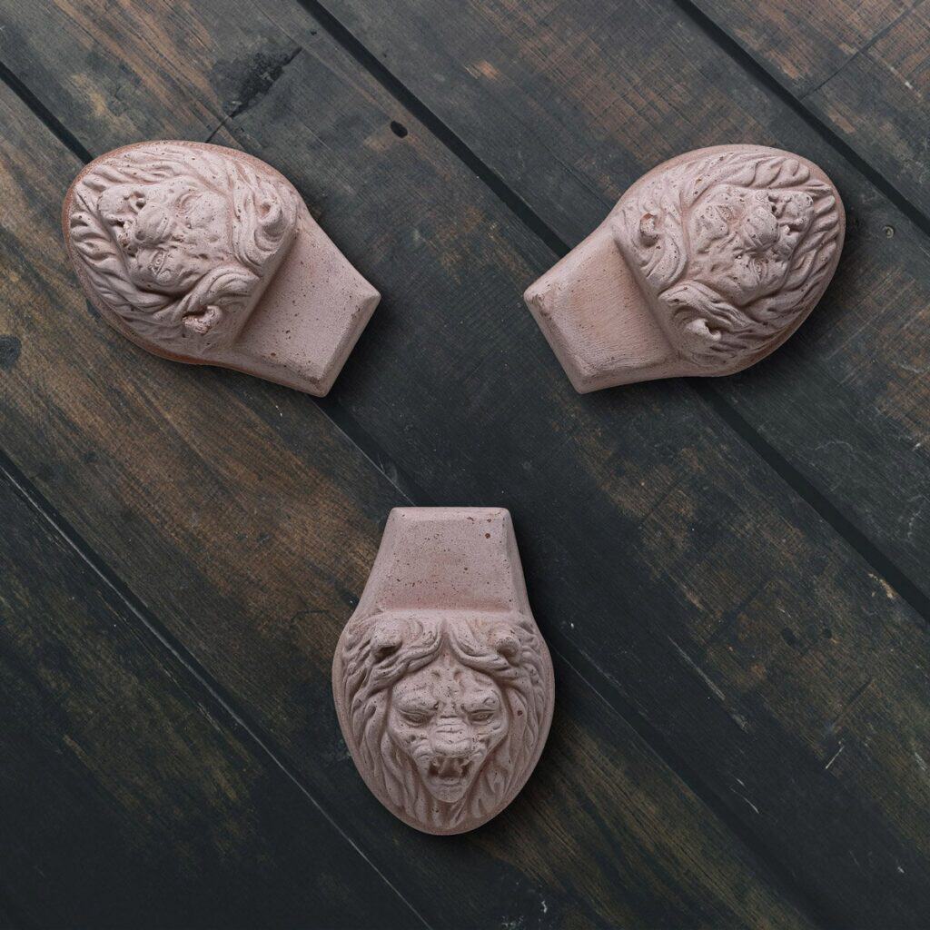 Tre krukfötter Lejonhuvud från Bergs Potter i terrakotta på mörkt träunderlag.