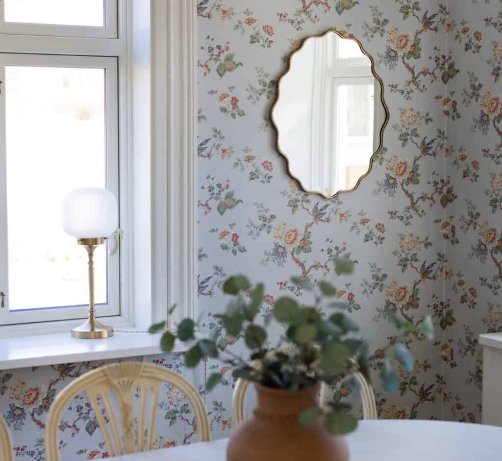 Lantlig matsal med blommig tapet, spegel, bordslampa och vas på bordet