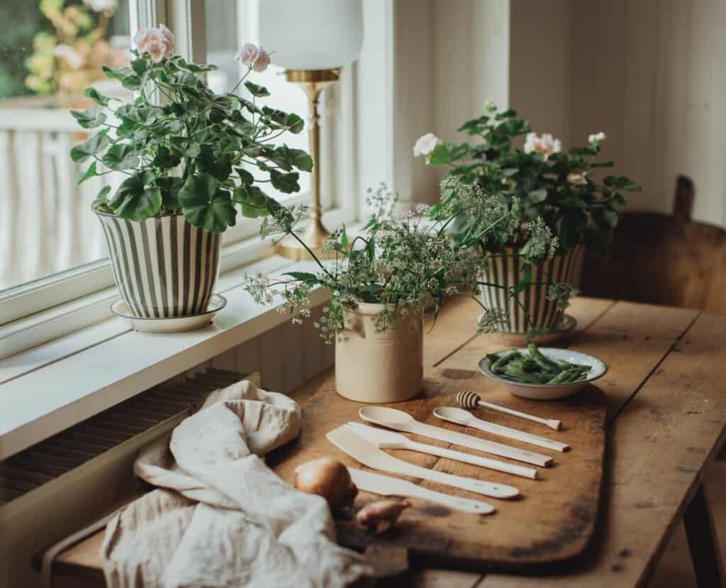 Lantlig sommarkänsla hemma med pelargoner i krukor, mjukt fönsterljus och träbord