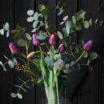 Konstgjord eukalyptus och lila tulpaner arrangerade i glasvas