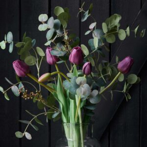 Konstgjord eukalyptus och lila tulpaner arrangerade i glasvas