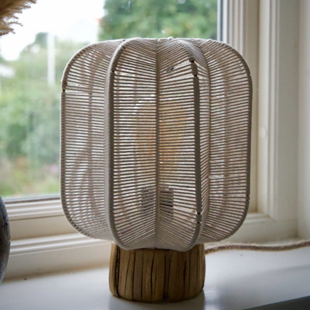 Bordslampa i offwhite bomullsrep med naturfärgad bas av sjögräs, placerad i ett fönster.