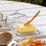 Smörbytta i glas på dukat frukostbord med smör och träkniv