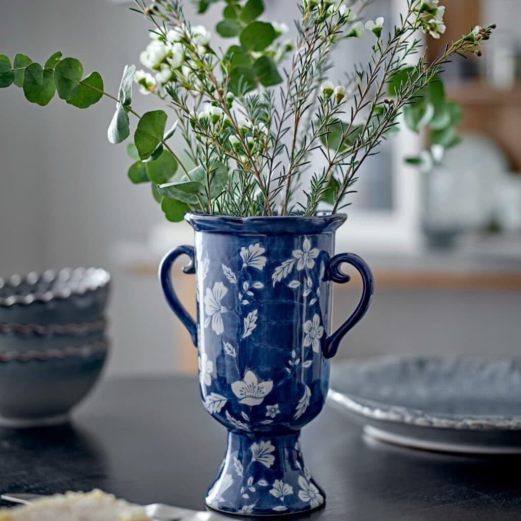 Amara blå vas i stengods med vita blommor och gröna kvistar på dukat bord