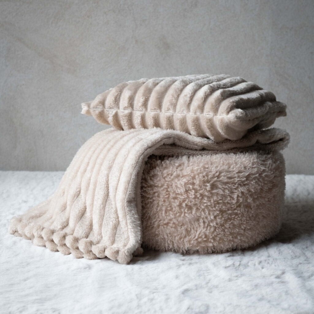 Beige Isla kuddfodral tillsammans med matchande pläd i mjuk ribbad textil