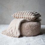 Beige Isla kuddfodral tillsammans med matchande pläd i mjuk ribbad textil
