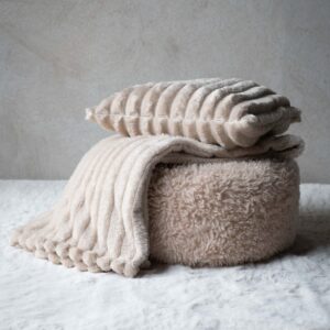 Beige Isla kuddfodral tillsammans med matchande pläd i mjuk ribbad textil