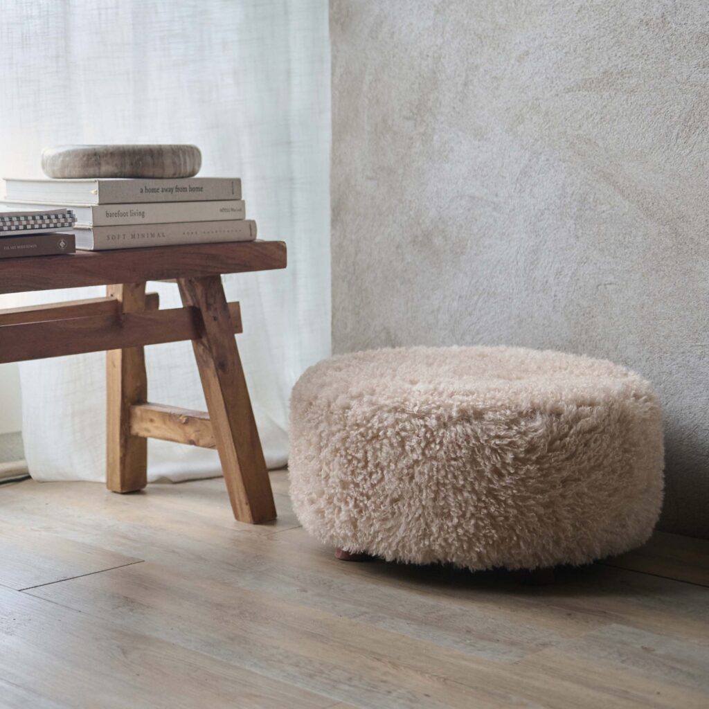 Rund sittpuff Leane i beige fluffig teddy från Wikholm Form bredvid en träbänk med böcker, ljus och vas i ett ljust rum.